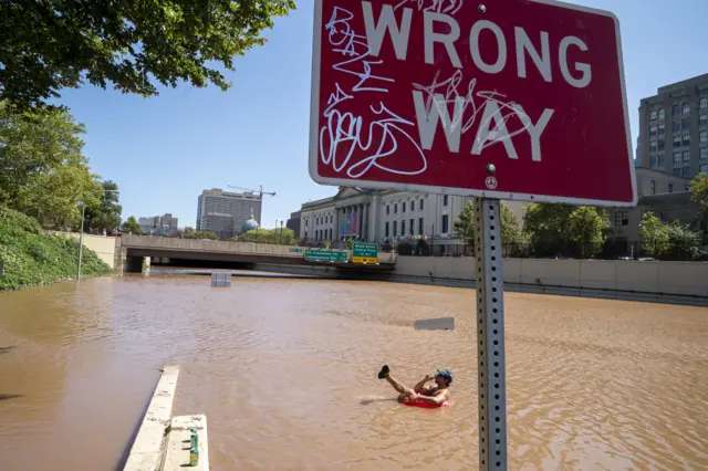 A man drinks a beer while floating on floodwater in Philadelphia, Pennsylvania