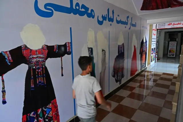 An Afghan youth walks past the wall of a shop with the images of women deface