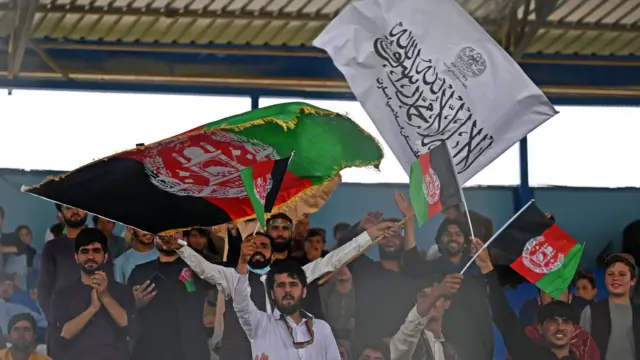 Spectators wave Afghanistan's and Taliban flags as they watch the Twenty20 cricket trial match being played between two Afghan teams 'Peace Defenders' and 'Peace Heroes' at the Kabul International Cricket Stadium in Kabul on September 3, 2021.