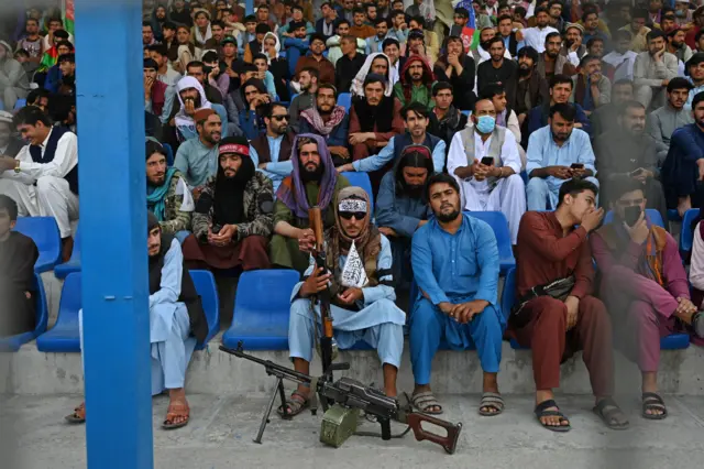 A Taliban fighter (C) keeps vigil as spectators watch the Twenty20 cricket trial match being played between two Afghan teams 'Peace Defenders' and 'Peace Heroes' at the Kabul International Cricket Stadium in Kabul on September 3, 2021.