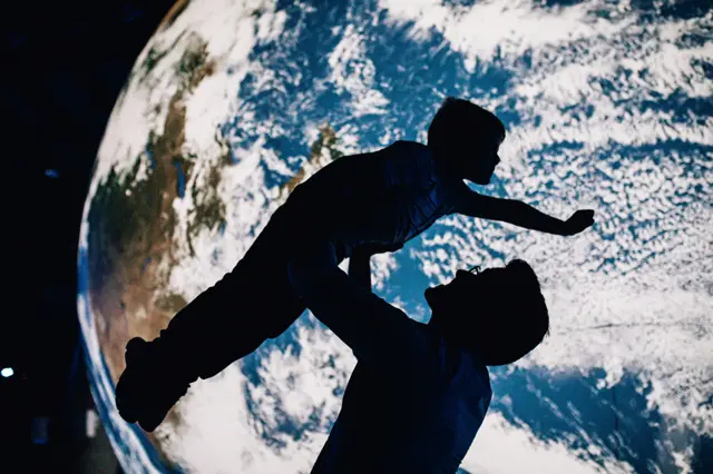 Father lifting son into the air with a giant replica Earth as a backdrop