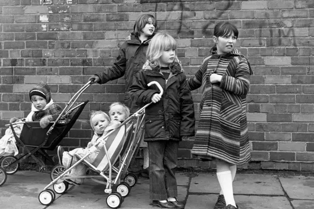 Children push prams along Hessle Road