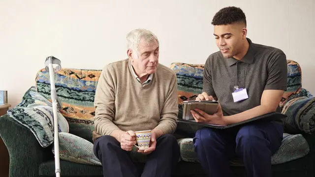 A young carer showing an elderly man something on an electronic tablet