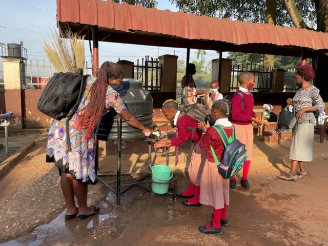 A teacher helps pupils wash their hands