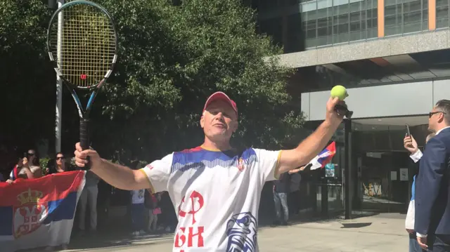 Djokovic fan Mick Mianovich holds up a tennis racquet and ball as hearings over the tennis star's entry visa into Australia are under way