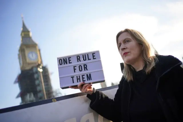 Protester holding sign saying "one rule for them" with Big Ben in background