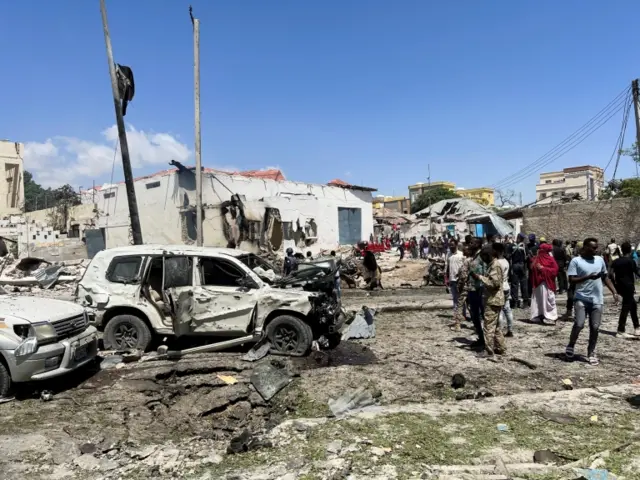 Civilians look at the wrecked vehicles at the scene of an explosion in the Hamarweyne district of Mogadishu, Somalia, January 12, 2022