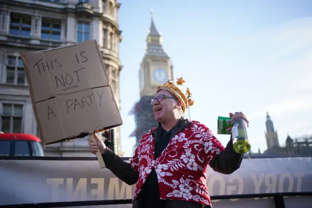 Protester holding wine bottle and "this is not a party" sign in Westminster