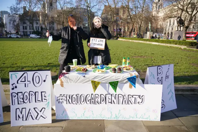 Two protesters with table of food and garden party sign in Parliament Square