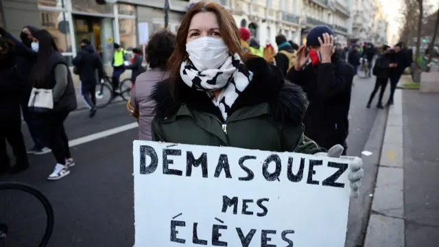 A woman wearing a protective face mask holds a placard reading "unmask my students" during a demonstration by French teachers as part of a nationwide day of strike and protests against sanitary conditions in schools, in Paris amid the rise of coronavirus disease (COVID-19) cases due to the Omicron variant in France,