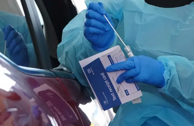 A member of staff performing a PCR test by a car