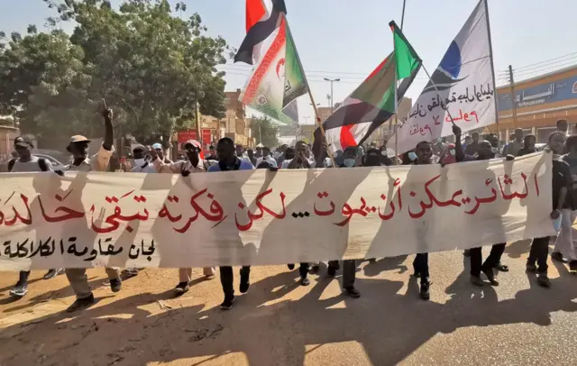 People hold a banner that says in Arabic: "The protester may die but his message remains eternal."