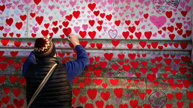 A man writes on a heart at the National Covid Memorial Wall, in Westminster, London.