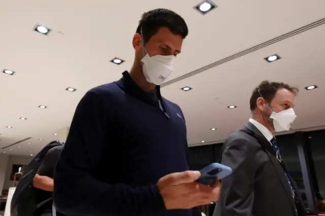 Novak Djokovic looks at his phone while walking through Melbourne Airport