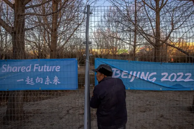 A worker attaches a banner on a fence, near the venues for the Beijing 2022 Winter Olympics