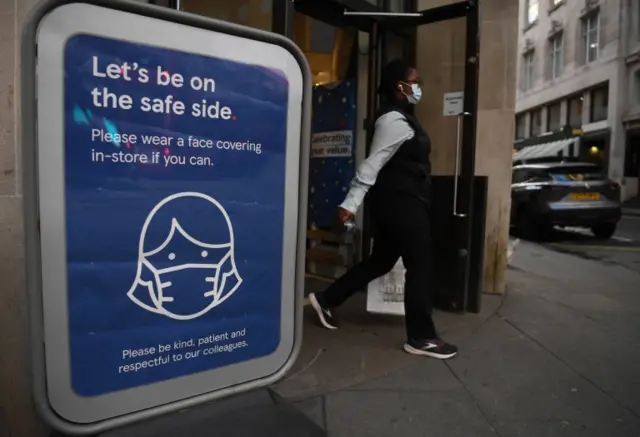 A masked woman passes COVID-19 guidance at a store in London, Britain, 19 January 2022.