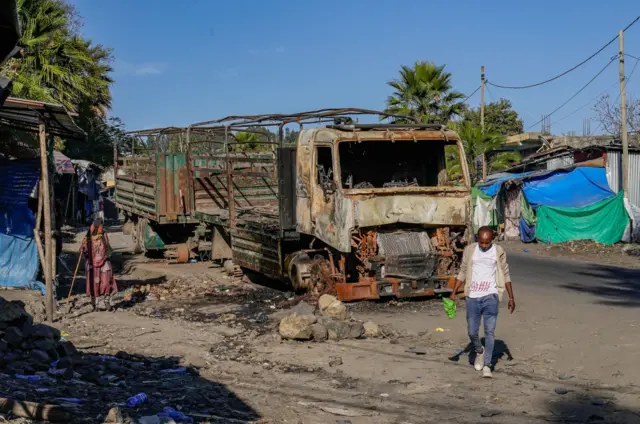 A man walks past the wreckage of a damaged vehicle on the A2 road in the city of Haik on January 12, 2022 in the Haik, Ethiopia. Haik is one of several towns and cities along the A2 road through the Wollo region that was occupied by the TPLF during its invasion of the Amhara region that started in July of 2021.