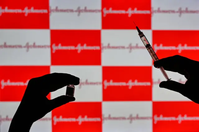 A stock image showing someone holding a vaccine syringe in front of the Johnson & Johnson logo.