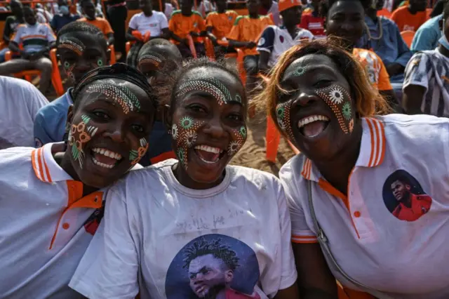 Three Ivory Coast's supporters pose as they wait to watch on a giant screen the Africa Cup of Nations (CAN) 2021 round of 16 football match between Ivory Coast and Egypt in a popular district of Abidjan on January 26, 2022.