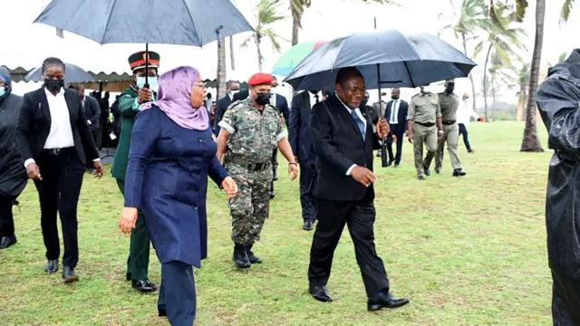 Tanzania President Samia Sululu Hassan (L) and President Filipe Nyusi (R) walking under umbrellas