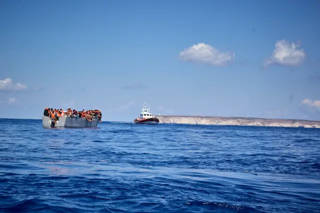 A dinghy carrying a total of 70 migrants (l) and a Lampedusa Coast Guard patrol boat (r), on September 8, 2021, in the Mediterranean Sea near Lampedusa