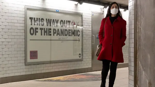 A woman in a mask walks past a sign saying "This way out of the pandemic"