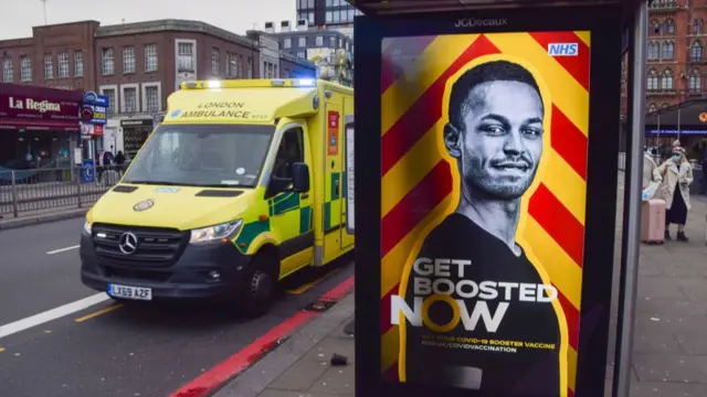 An ambulance drives past an advert urging people to get a Covid-19 vaccine booster shot at a bus stop in London