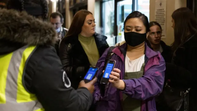 A woman shows her Covid pass to someone in a hi-vis vest