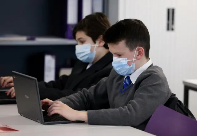 Two school children sit at their desks wearing face masks