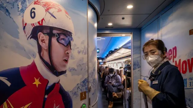 Inside a high speed train decorated with winter sports branding and person wearing a face mask