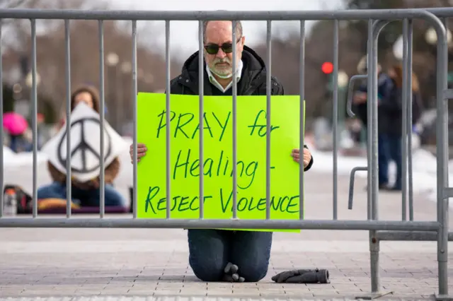 A protester outside Congress holds a sign reading "pray for healing, reject violence"