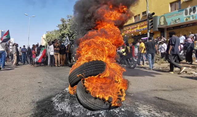 Tyre on fire, protesters in background