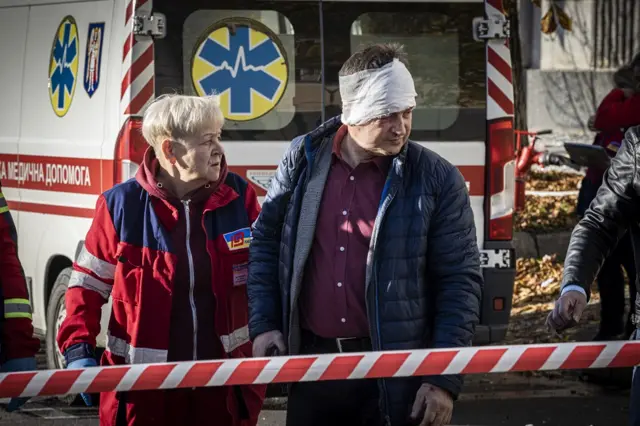 A wounded man walks past as emergency service personnel attend to the site of a blast on October 10, 2022 in Kyiv, Ukraine.