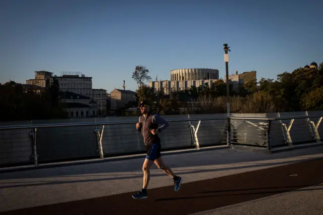 People run on the glass bridge in Kyiv as the sun rises on 8 October 2022 in central Kyiv, Ukraine