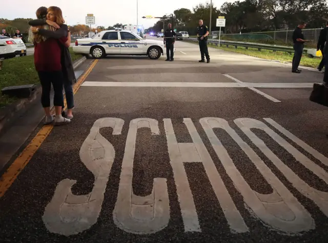 Police stand outside Marjory Stoneman Douglas High School in Florida while two women hug in front of caution tape