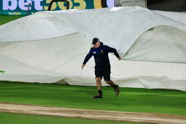 A groundsman helping to put the covers on during a rain delay