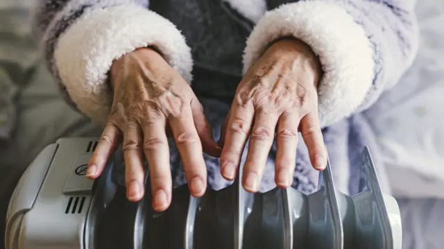 An elderly woman places her hands over an electric heater