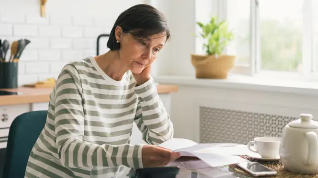 A woman looking at a bill while sitting at her kitchen table