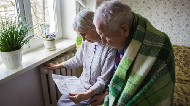 A woman holding gas bill in front of heating radiator