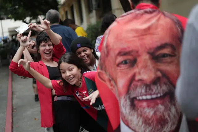 Supporters of ex-president Lula queue to vote in Rio de Janeiro draped in his party's colour - red - and in a giant towel stamped with the left-wing candidate's face