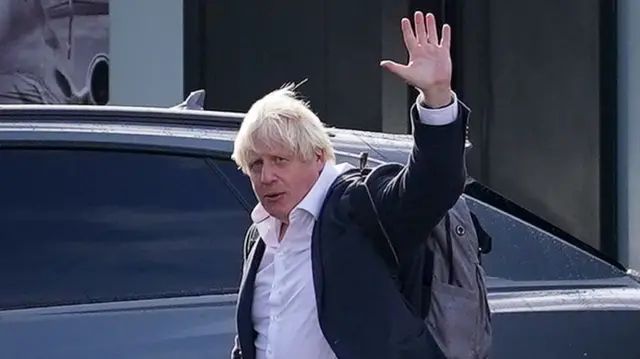 Boris Johnson waves to reporters as he arrives at Gatwick earlier