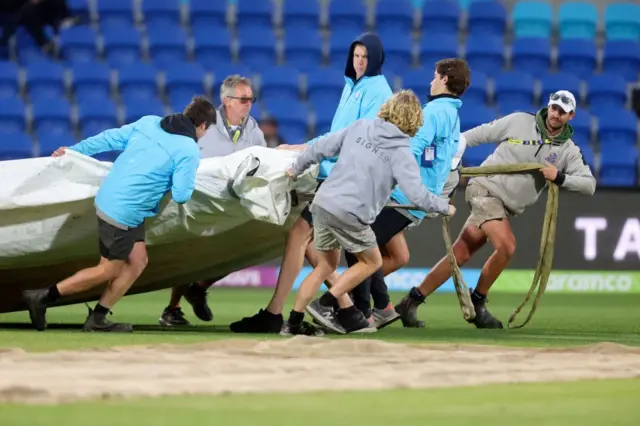 The groundstaff putting the covers on