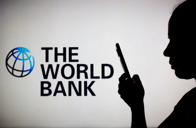 A woman's silhouette holds a smartphone with the World Bank logo in the background.