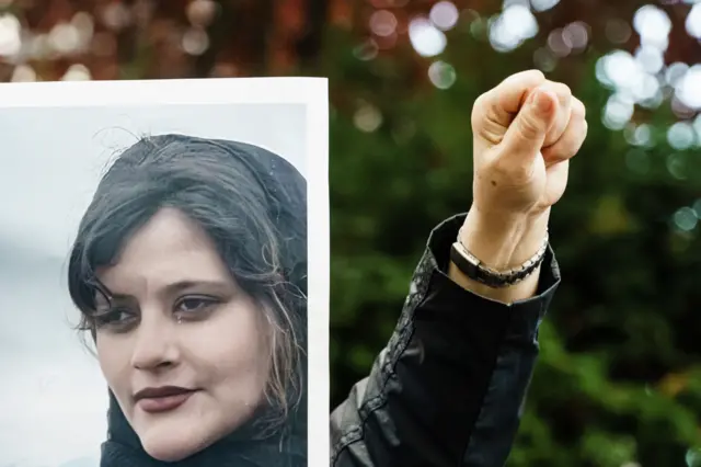 A picture of Mahsa Amini with a protestors fist up in the air