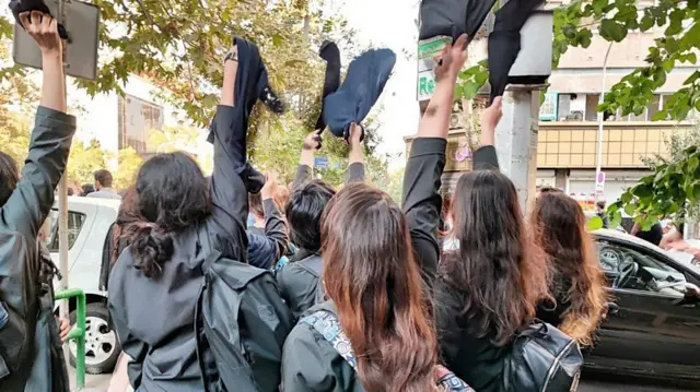 Young women holding their headscarves above their heads in protest