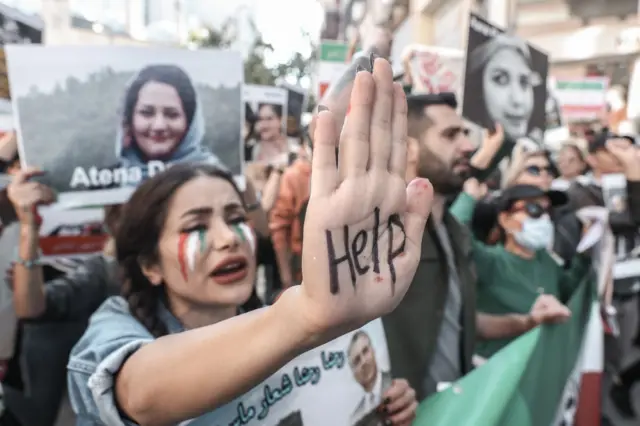 A woman with a poster and face paint with 'help' painted on her hand