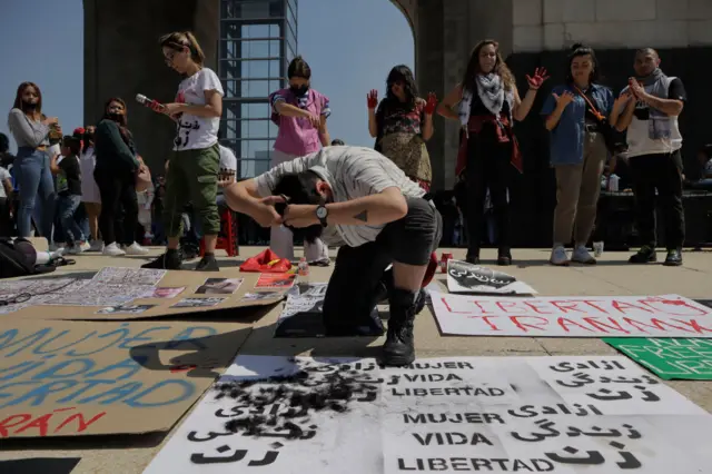 A woman cutting her hair over protestors posters on the ground