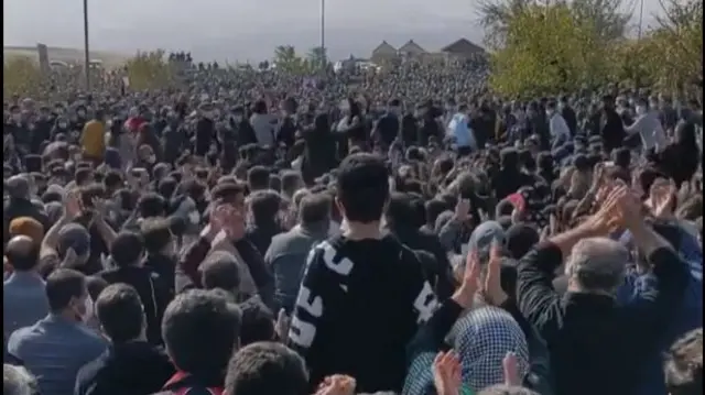 A large crowd of people as far as the eye can see. Some standing and clapping, some sitting.