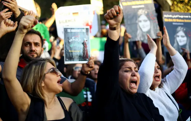 Women and men looking angry and upset as they hold up posters in support of Mahsa Amini