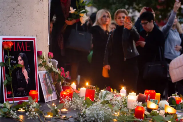 Candles and an image of Mahsa Amini with mourners in the background